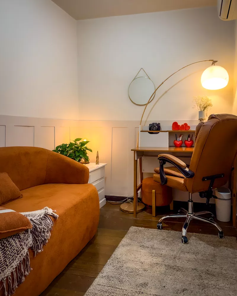 Sala com sofá caramelo, mesa, cadeira e luminária de piso.